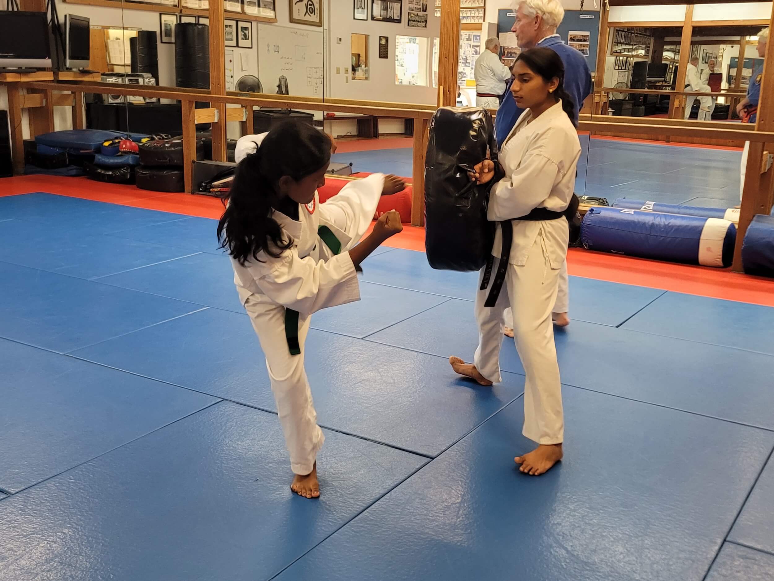 Community Martial Arts students kicking sparring equipment during class wearing uniforms.